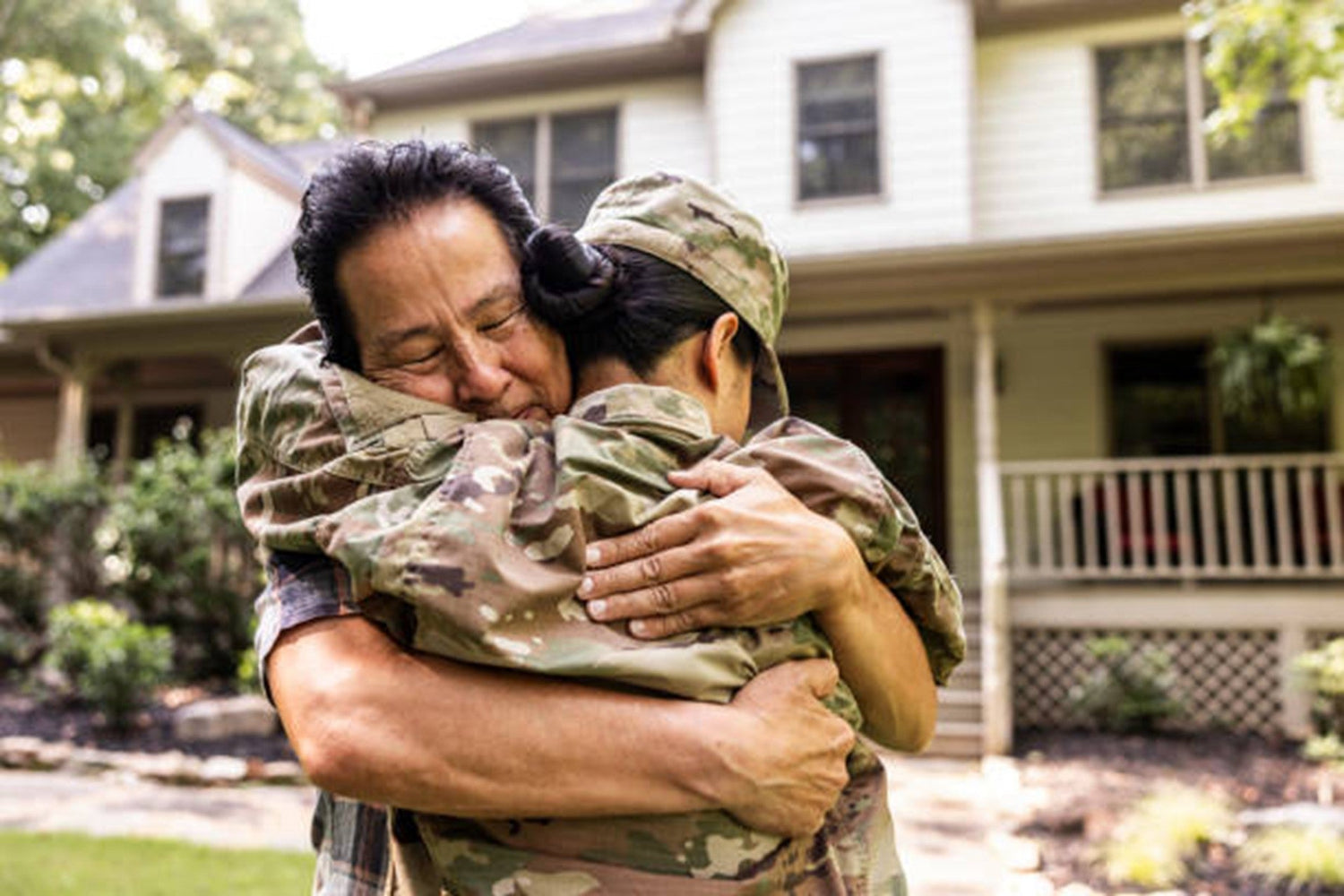 A girl in a soldier’s uniform is hugging an old man while standing in front of the house.